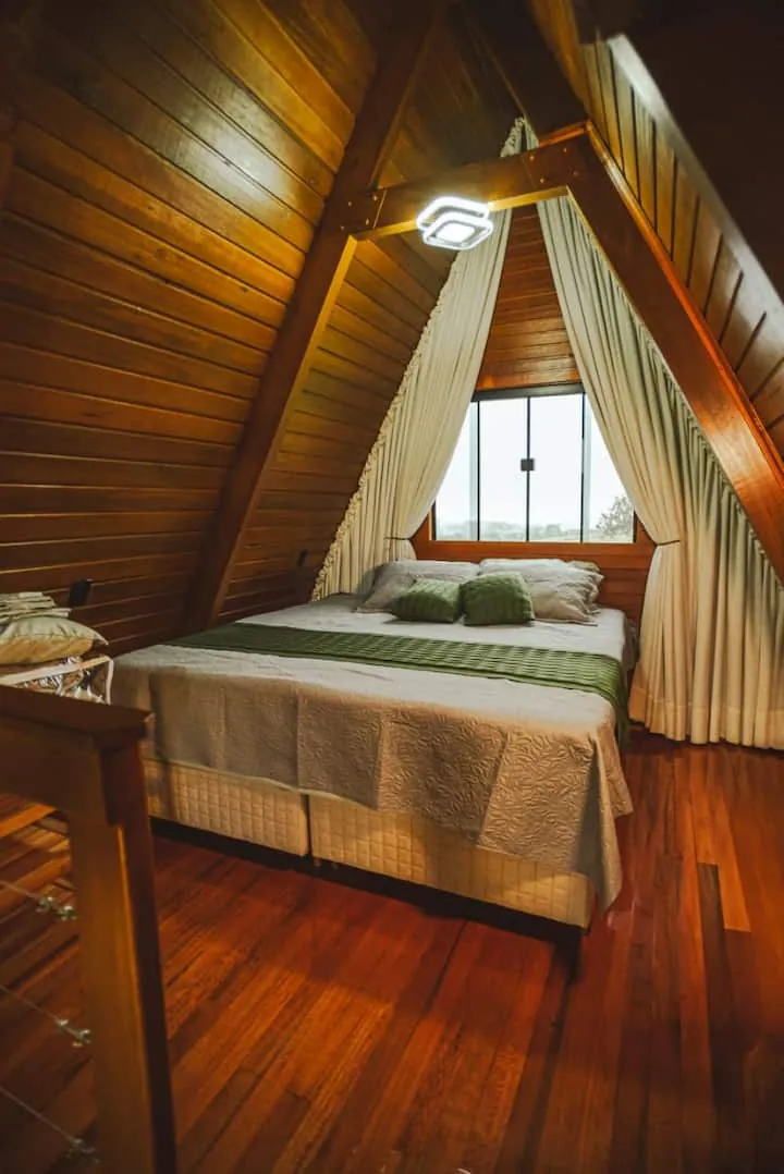 Quarto com cama king sob o telhado de madeira